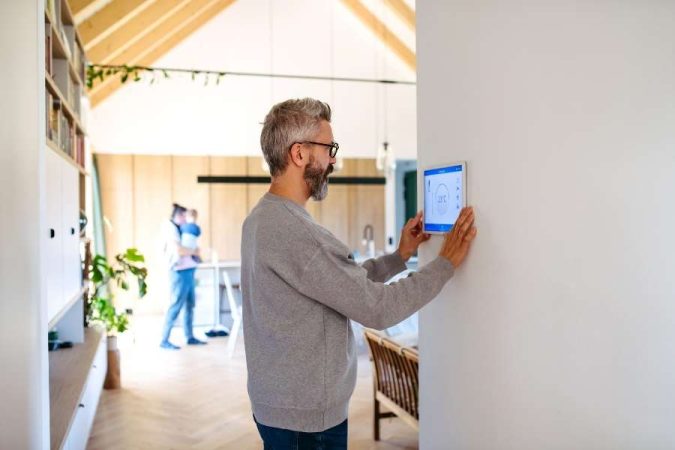 Un homme ajuste la température de son chauffage connecté sur une tablette murale dans sa maison moderne.